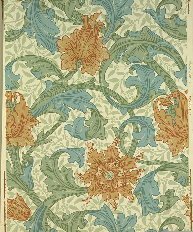 Single Stem Morris and Co wallpaper Flowers and scrolling foliage with pale foliage arabesque underlay. Printed in orange, blue and green on cream ground.