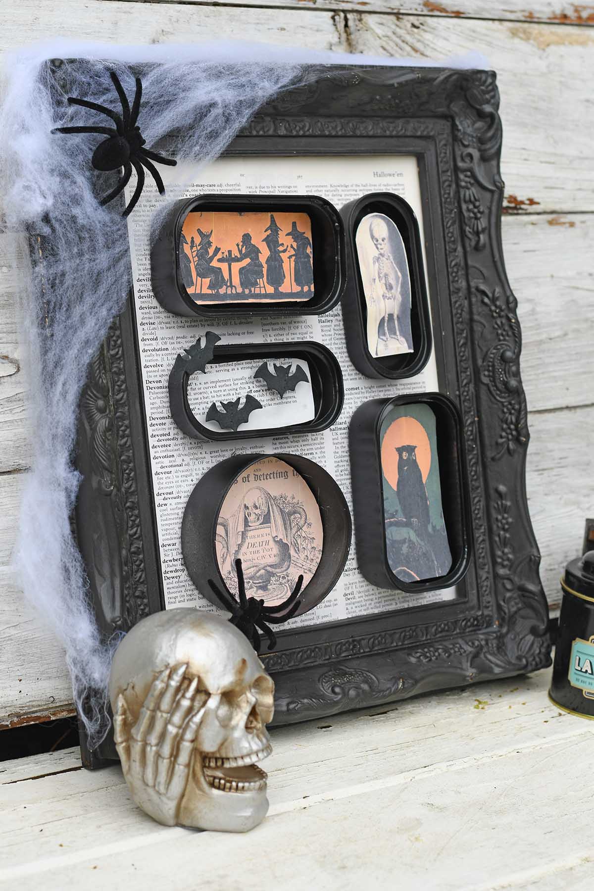 DIY Halloween shadowbox diorama with tin cans and vintage images, with small skull and black tin on wood background